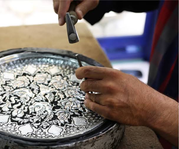 Artisan hand-engraving a decorative metal plate with a chisel