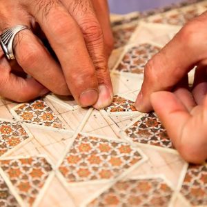 Close-up of hands placing khatam pieces into a geometric pattern