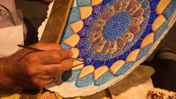 Painter decorating a blue minakari plate by hand