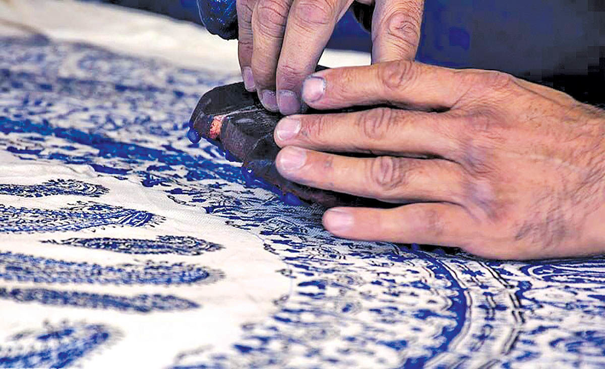 Hands pressing a carved wooden block onto qalamkar textile